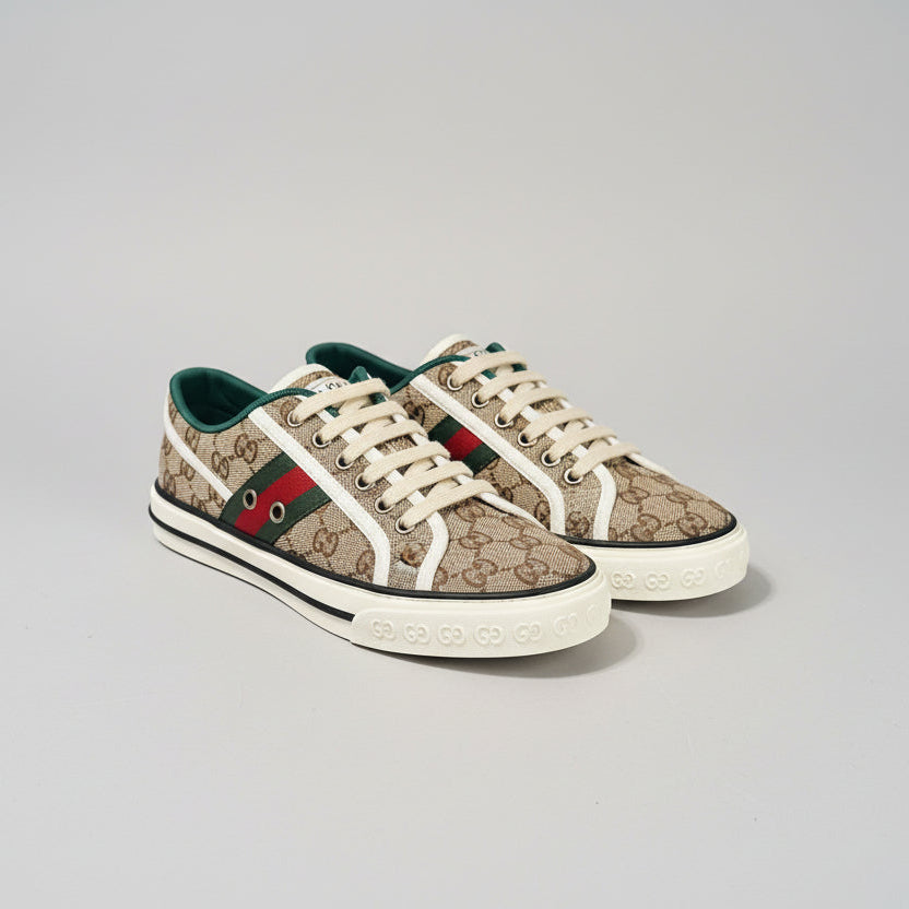 Pair of Gucci sneakers on a dark surface with a patterned box in the background.
