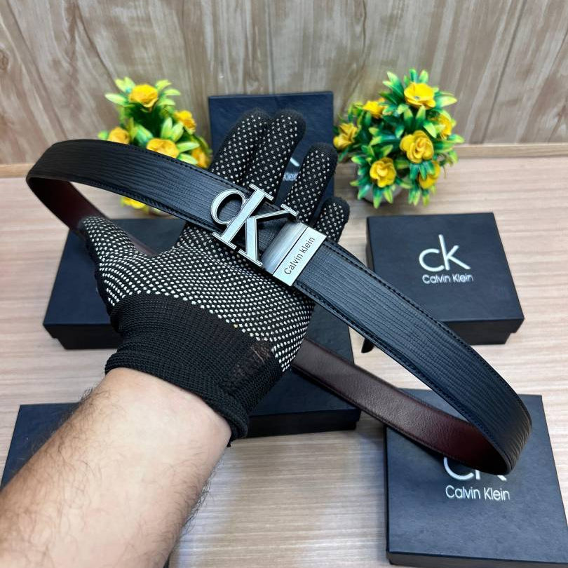 Calvin Klein belt and gloves on a wooden surface with branded boxes and small plants.