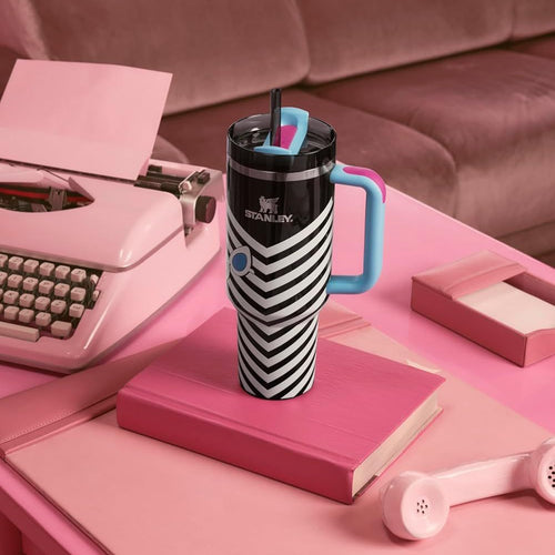 Black and white striped mug with blue handle on a pink desk with typewriter and notebook