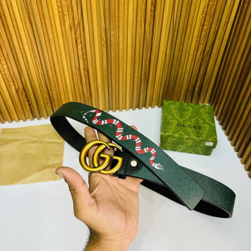 Hand holding a Gucci belt with a green strap and red snake design, against a wooden background.
