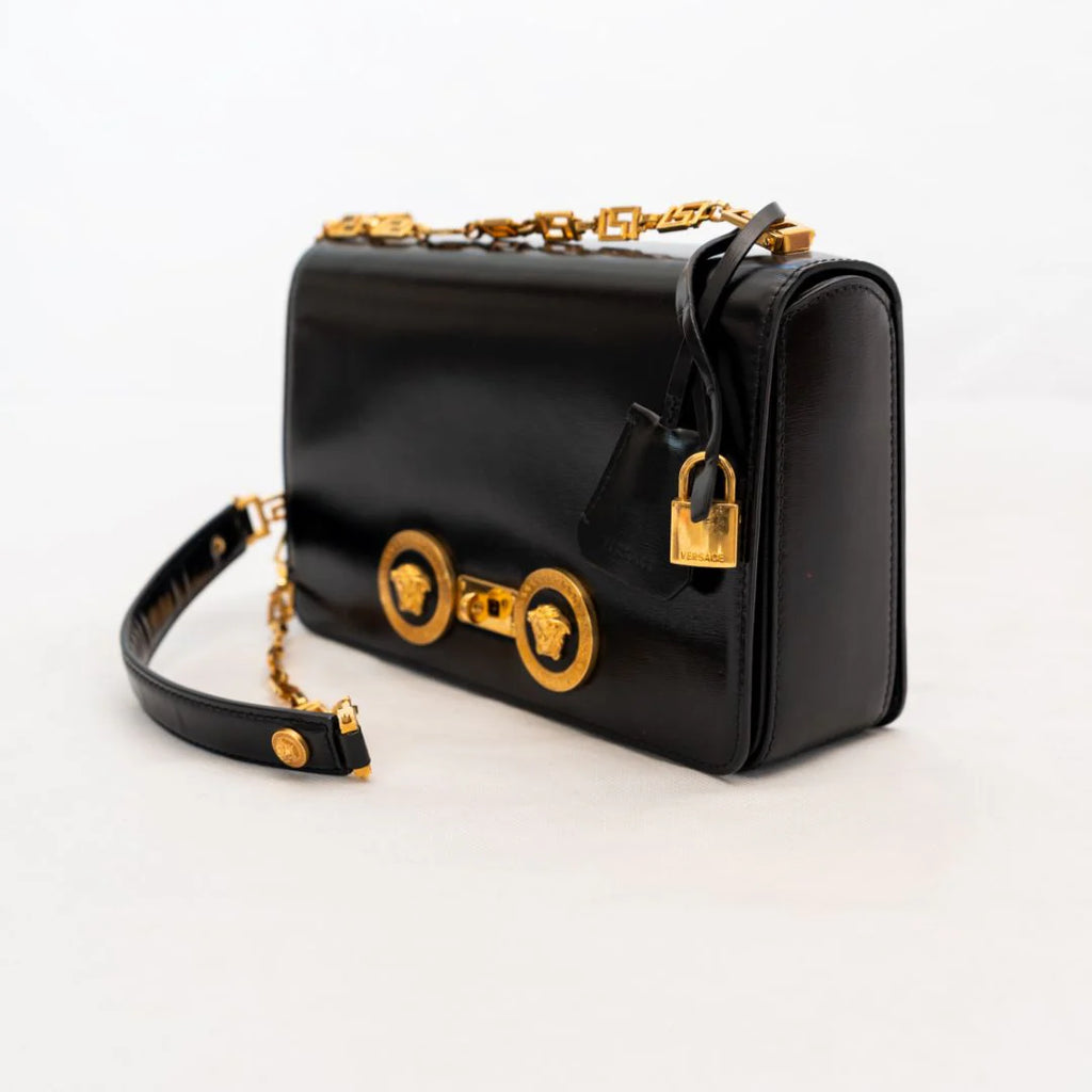 Black medusa handbag with gold accents on a white background