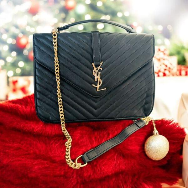 Black YSL Saint Laurent Premium Shoulder Bag handbag with gold chain on a red surface with Christmas decorations in the background