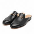 Black  Gucci mulesslip-on shoes with gold accents on a light gray background