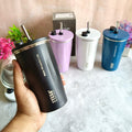 Black tumbler held by a hand with other colored tumblers in the background on a light surface.