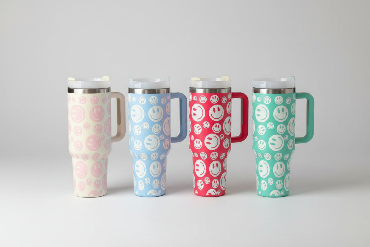 40 oz Stainless Steel Insulated Tumbler with Handle and Smiley Face Design – Durable Travel Mug with Straw Lid Four tumblers with smiley face patterns on a wooden surface