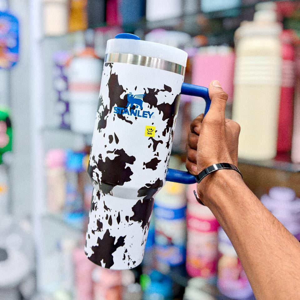 Person holding a cow print tumbler with a blue handle in a store setting