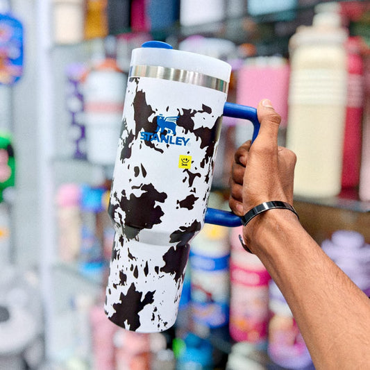Person holding a cow print tumbler with a blue handle in a store setting