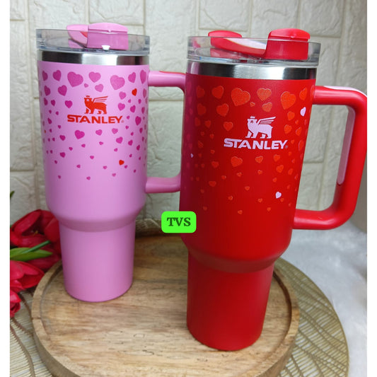 Two Stanley tumblers, one pink and one red, on a wooden surface with a light gray background.