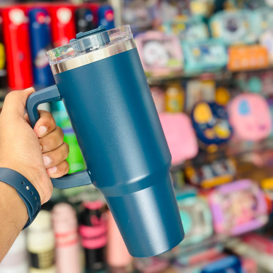 Blue insulated mug held by a hand with a store shelf in the background