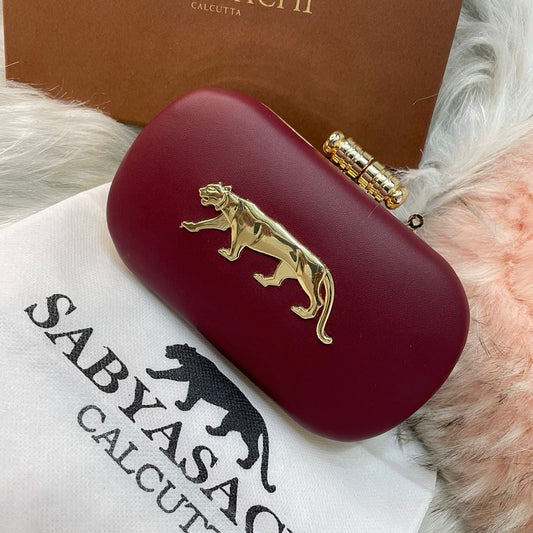 Red clutch with gold tiger emblem on a Sabyasachi branded box and towel.