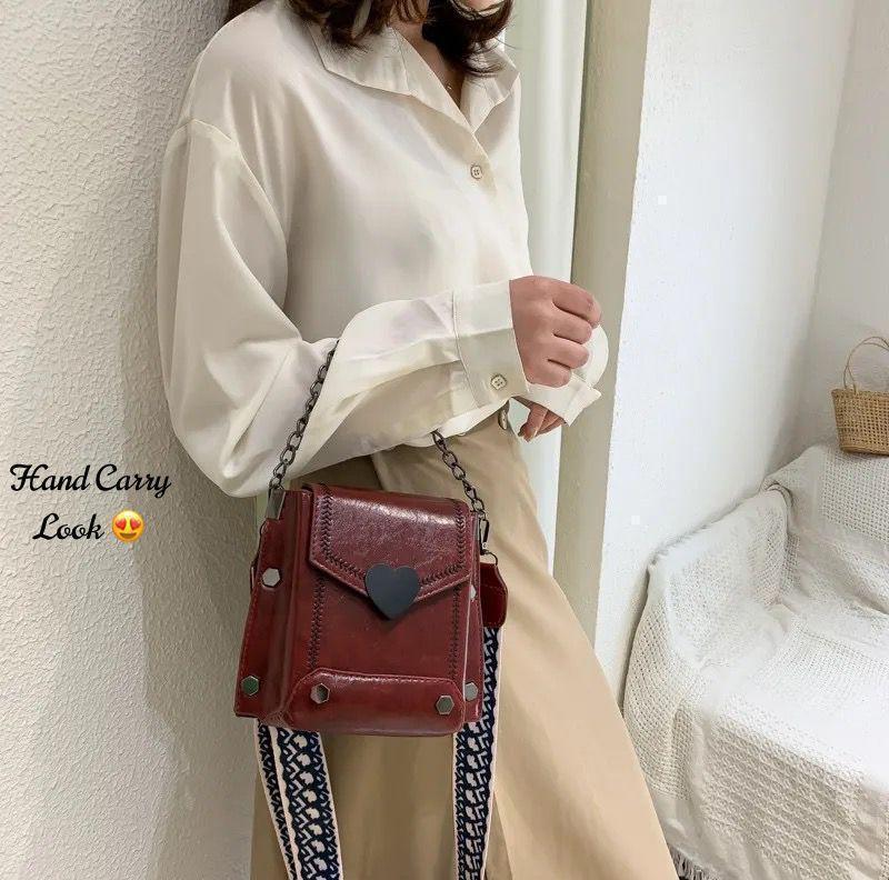 Person wearing a white shirt and beige pants with a red handbag, standing against a neutral wall.