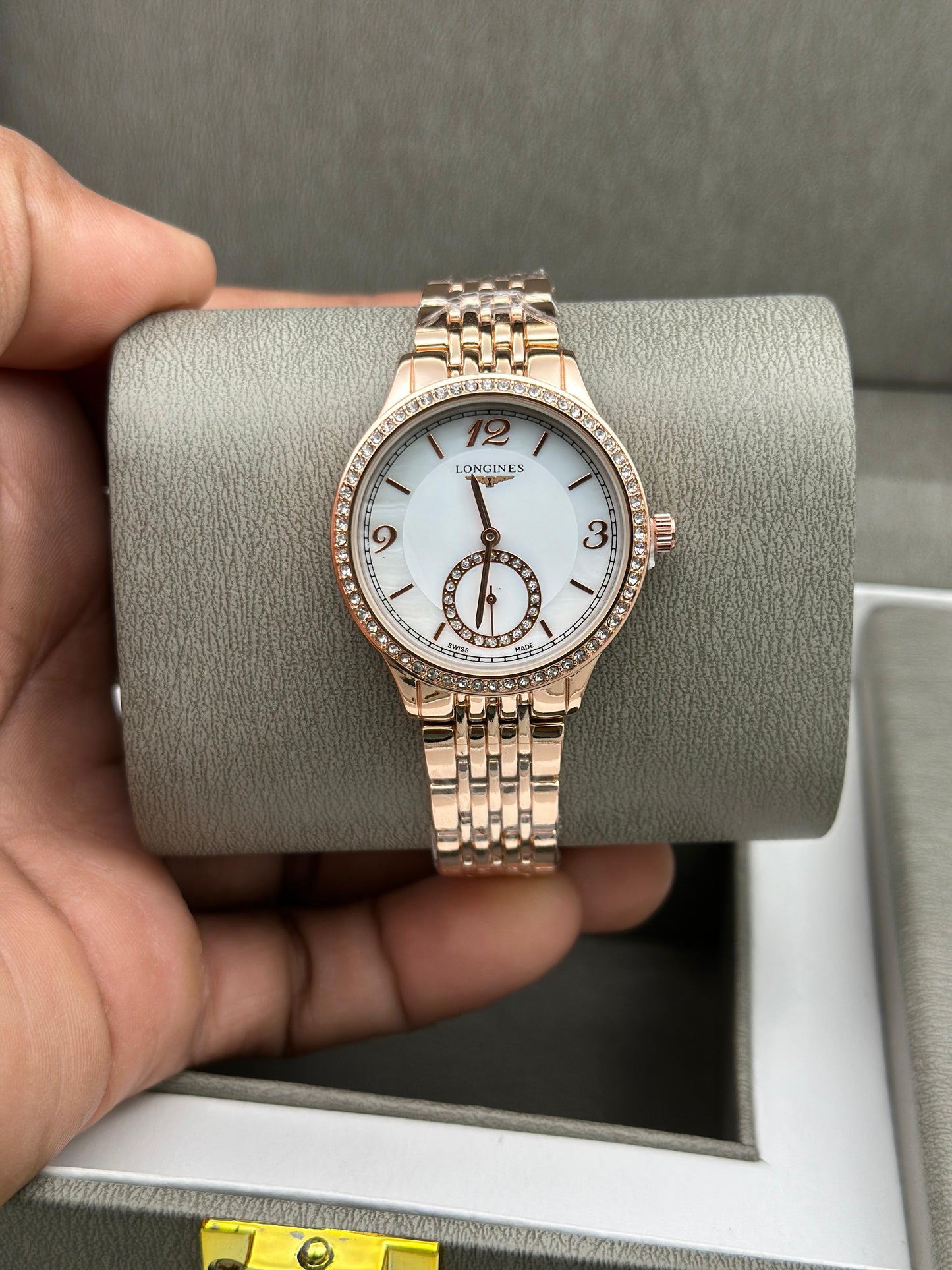 Rose gold watch held by a hand on a gray cushion with a gray background