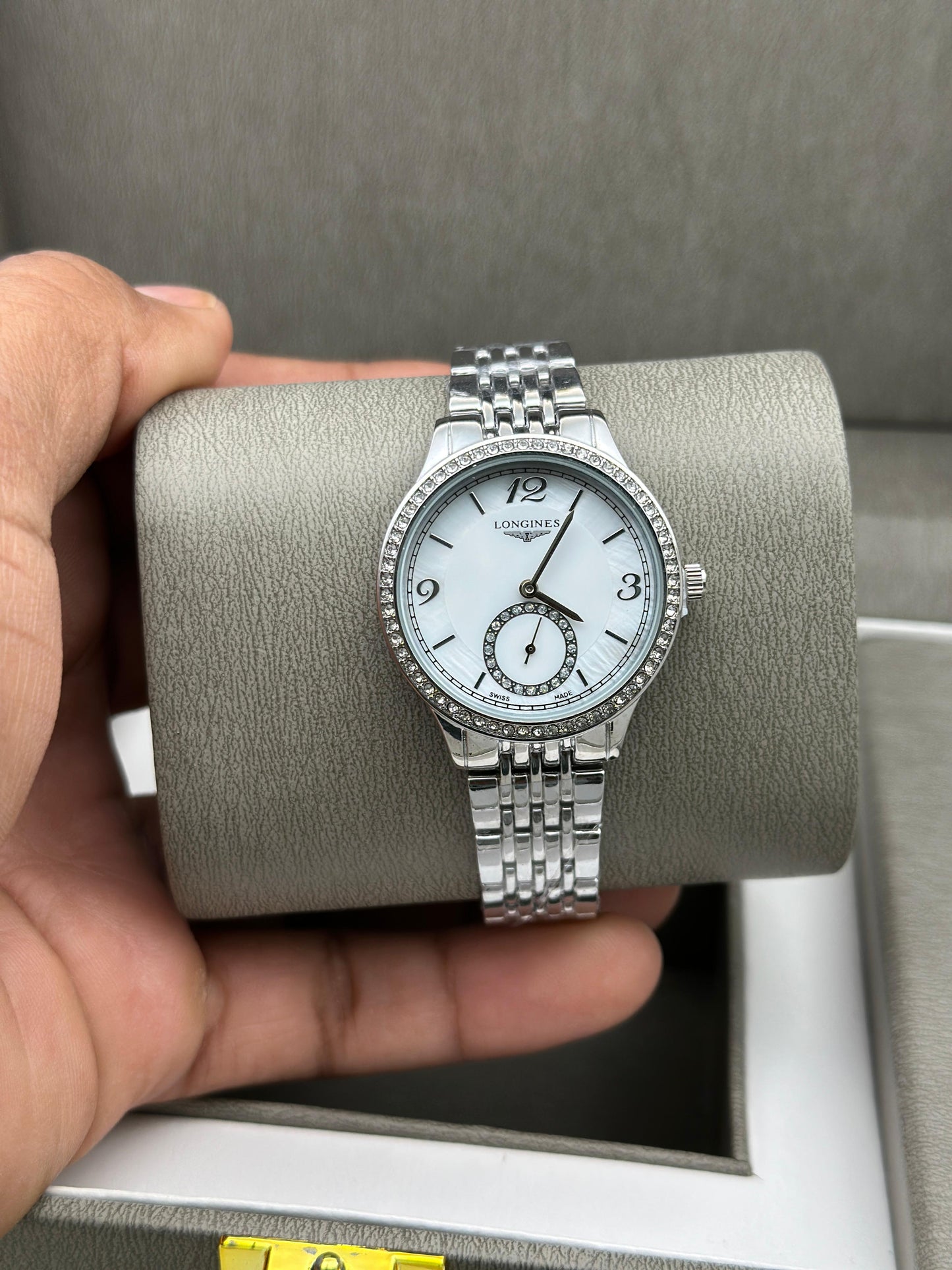 Silver watch on a gray cushion held by a hand with a neutral background