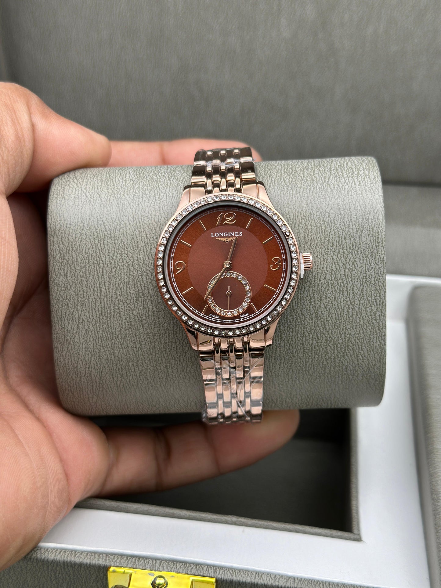 Rose gold watch with brown dial held by a hand on a gray cushion