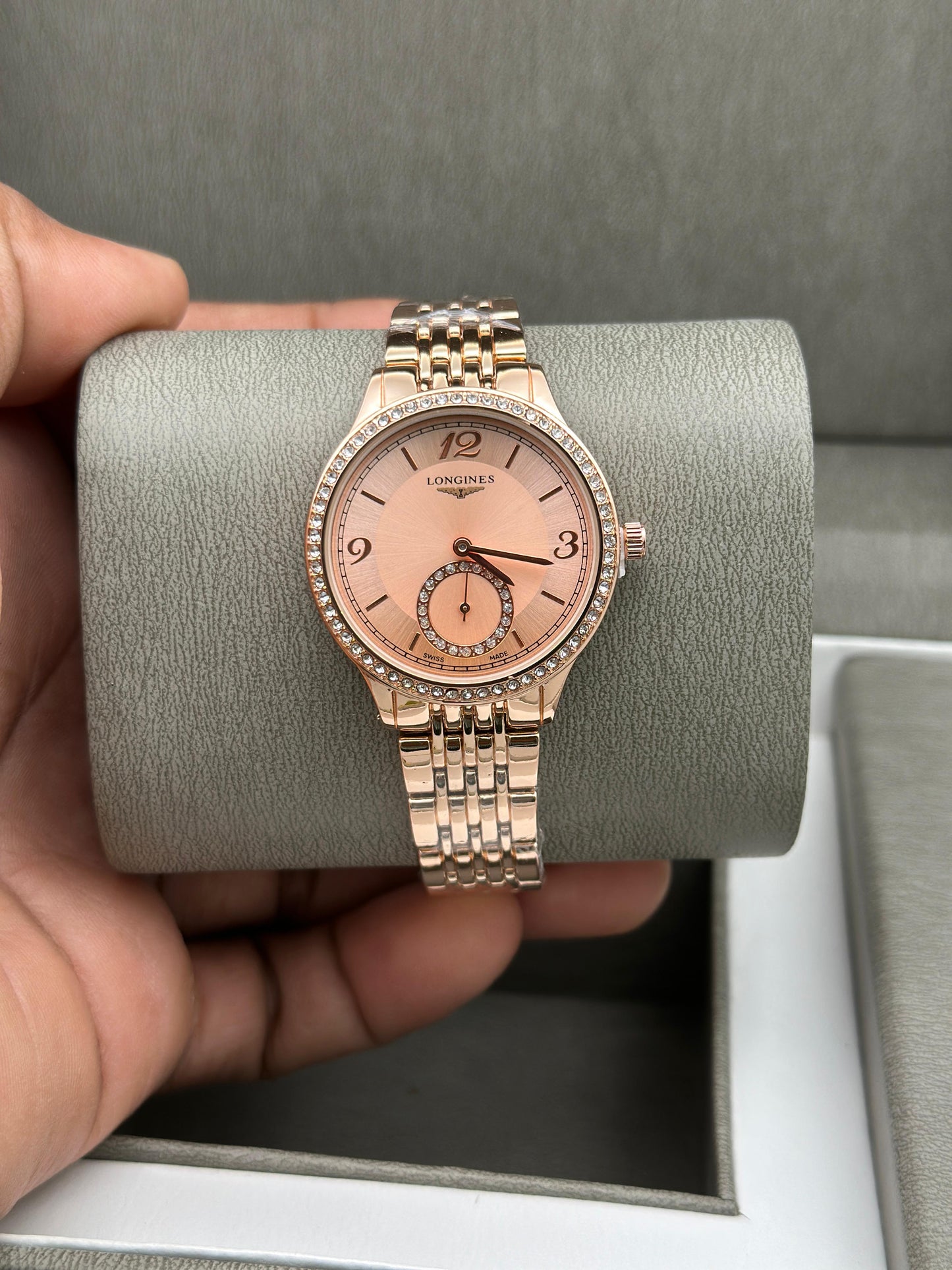 Rose gold watch held by a hand on a gray background