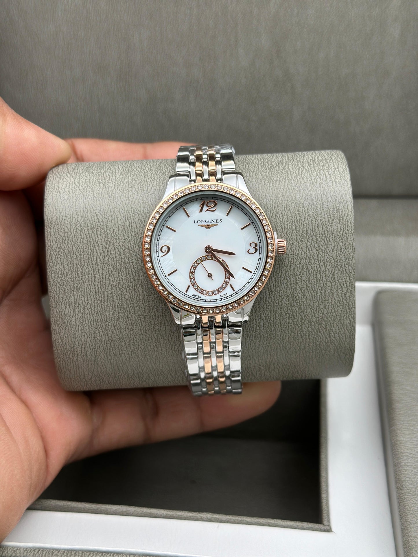 Two-tone watch held over a gray cushion with a blurred background