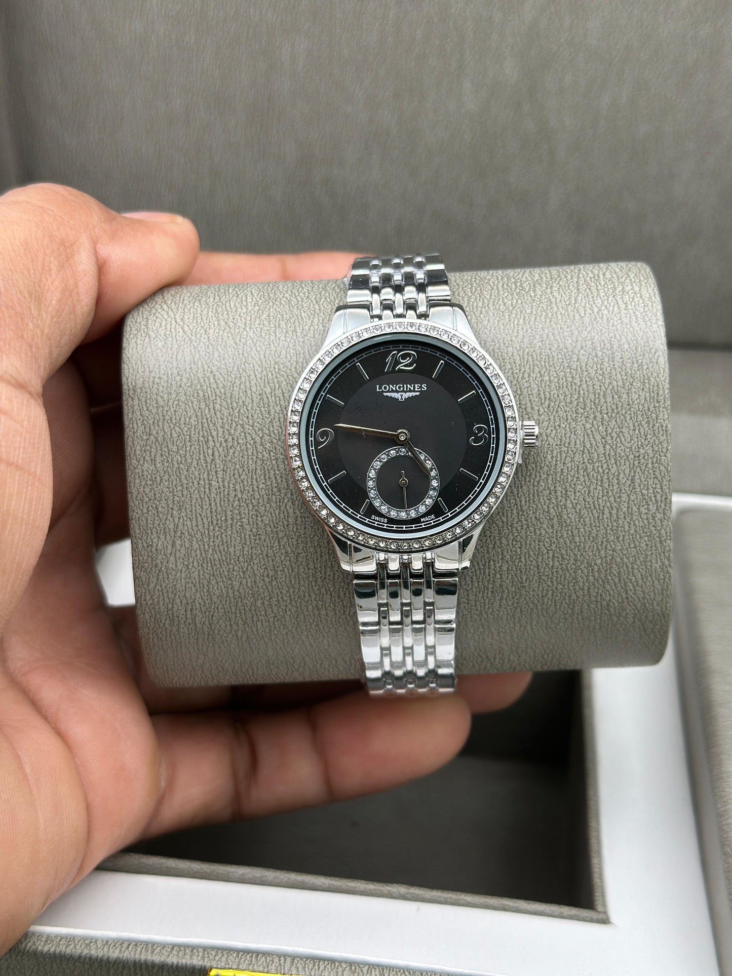 Silver watch with black face held by a hand on a gray background