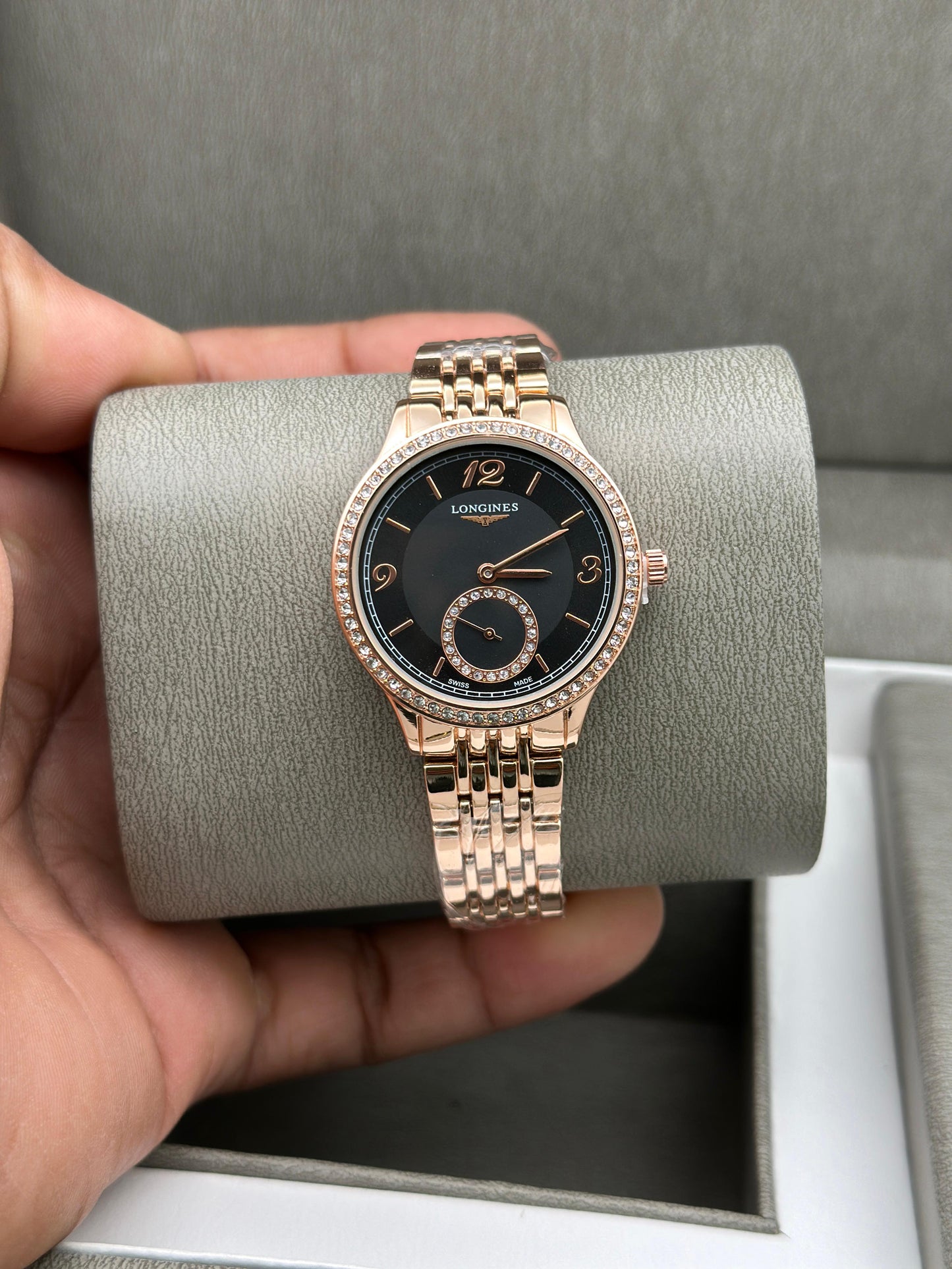 Rose gold watch with black dial held by a hand on a gray cushion