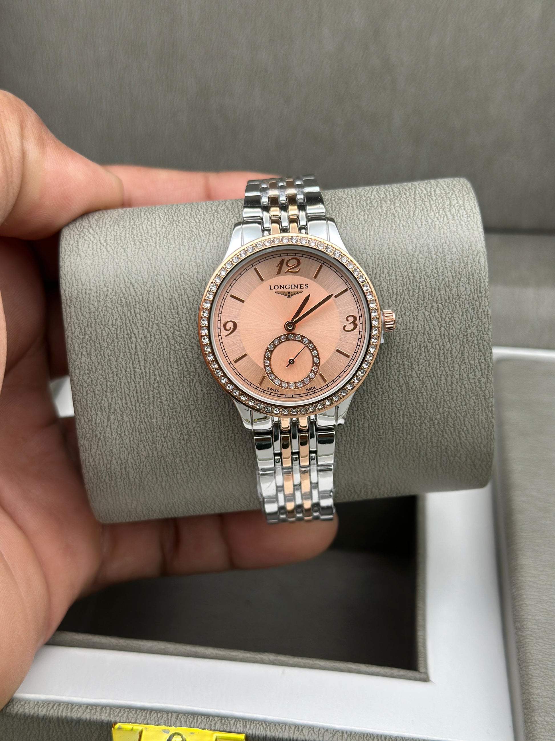 Silver and rose gold watch held by a hand on a gray cushion
