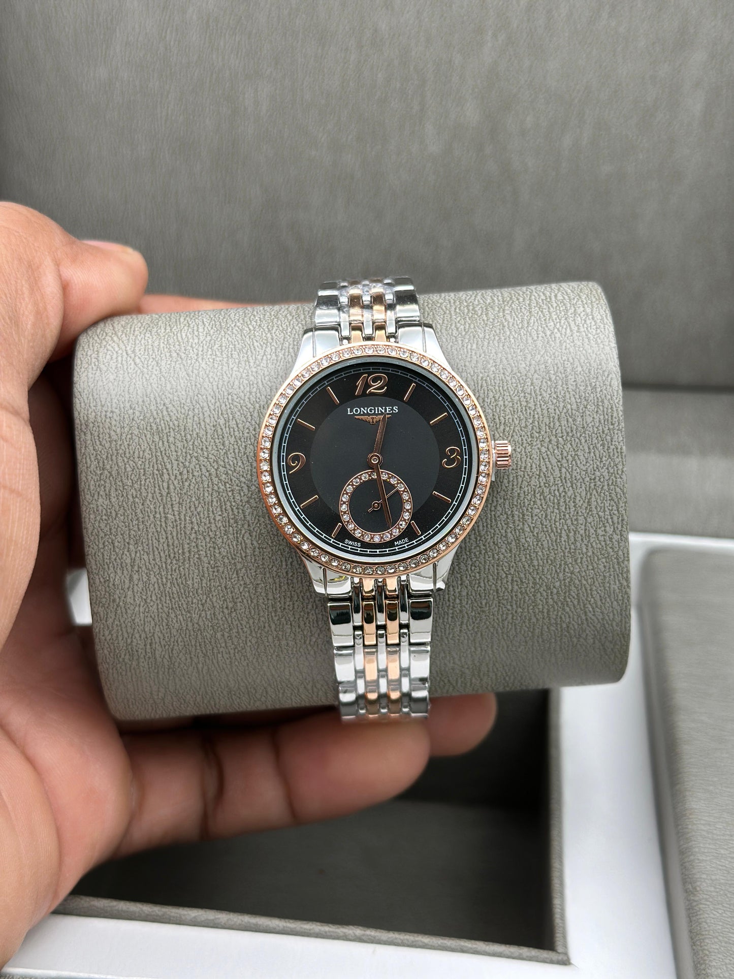 Luxury watch with silver and rose gold band held by a hand on a gray background