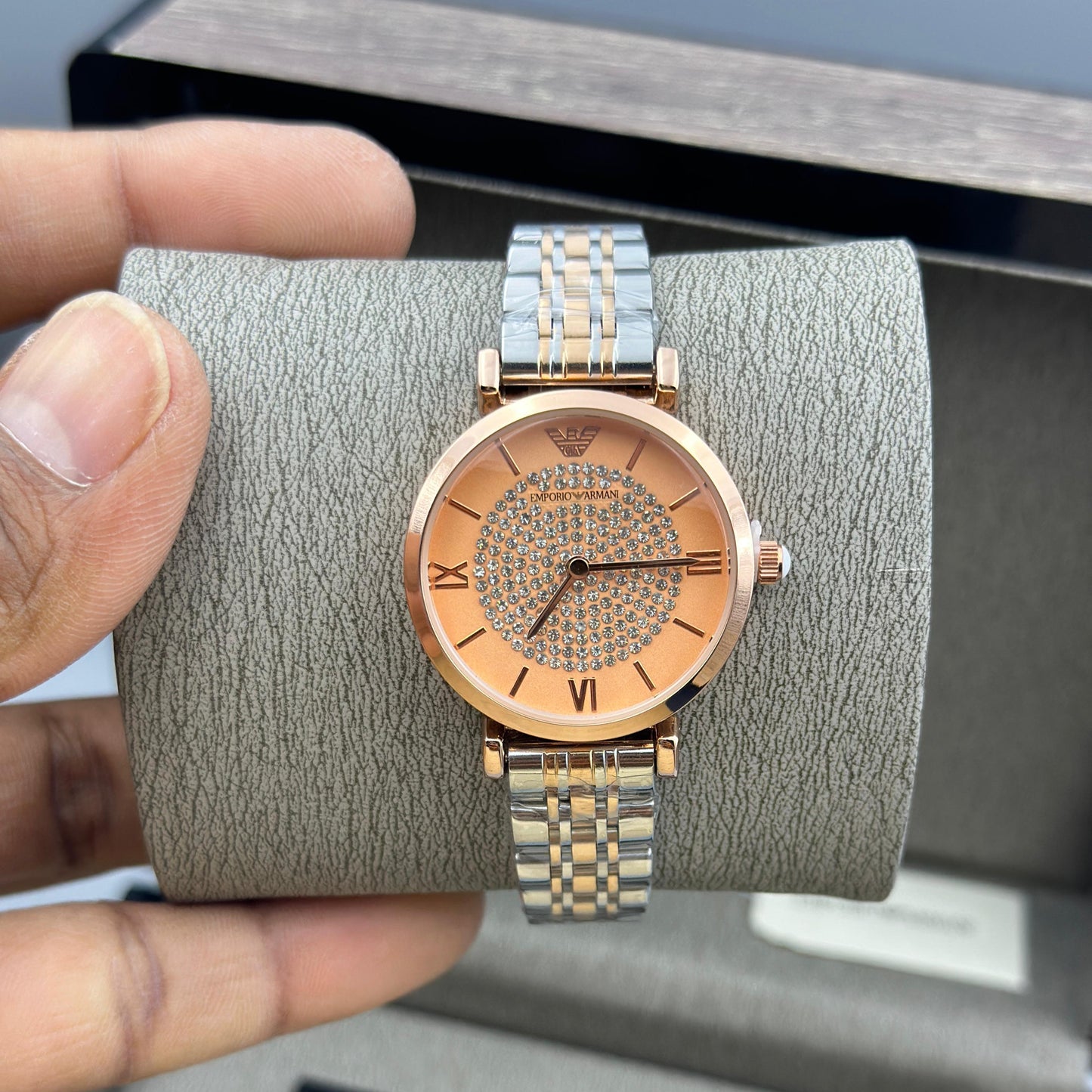 Gold watch on a gray cushion held by a hand with a gray box in the background