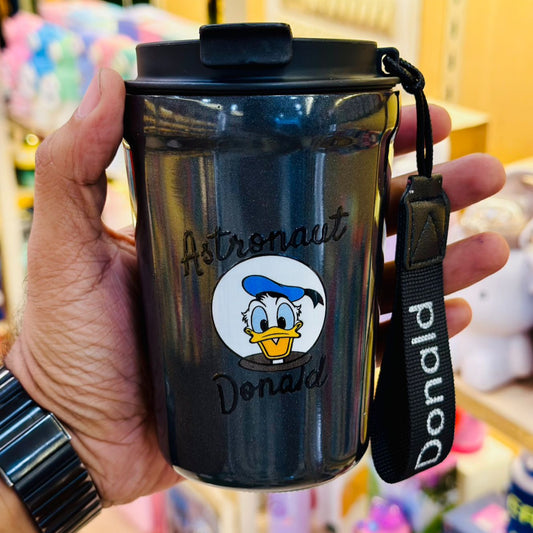 Black tumbler with Donald Duck design held by a person, against a blurred colorful background.