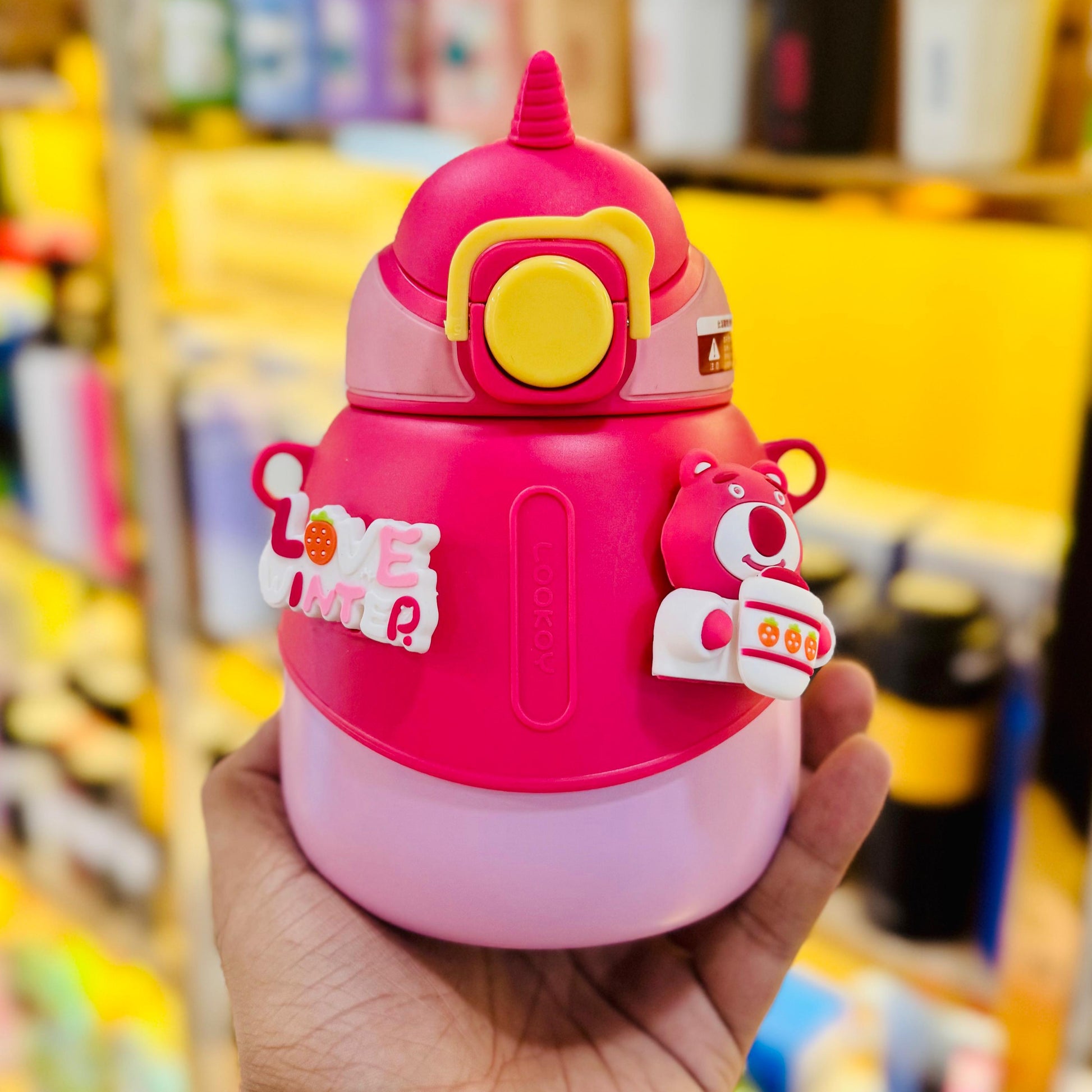 Pink cartoon-style water bottle held in a hand with a blurred store background