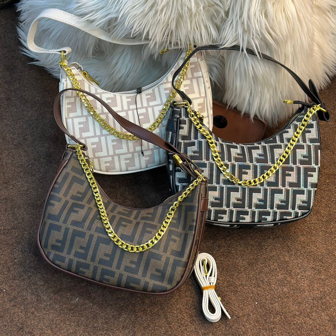 Two handbags with gold chains on a brown surface with a white fluffy blanket in the background.