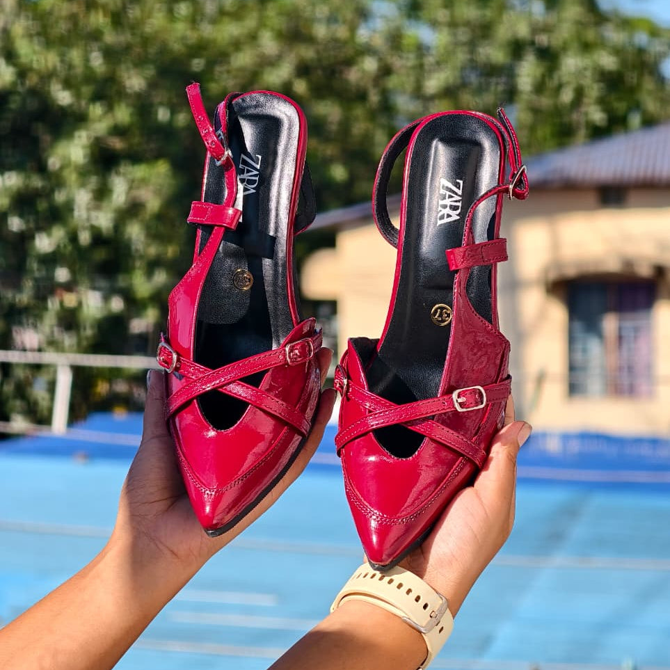 Red high-heeled shoes held by a person with a blurred outdoor background