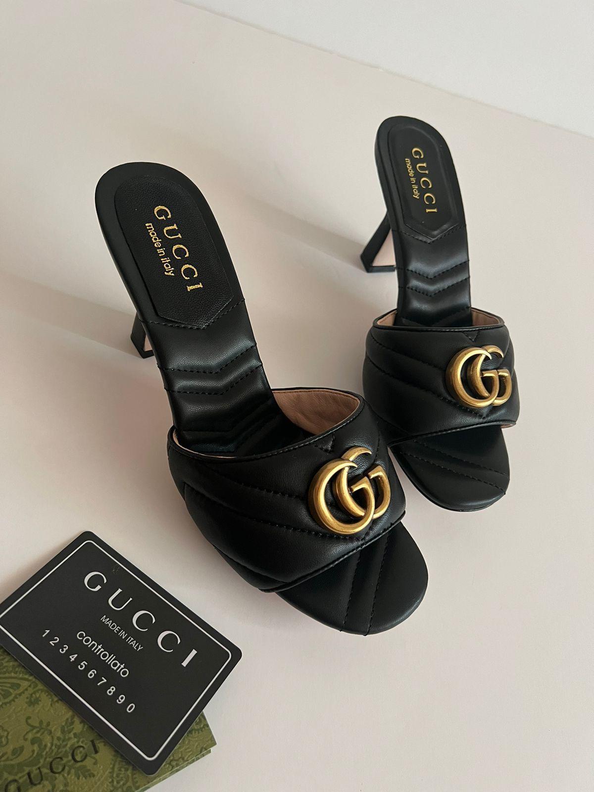 Black Gucci sandals with gold logo on a light background