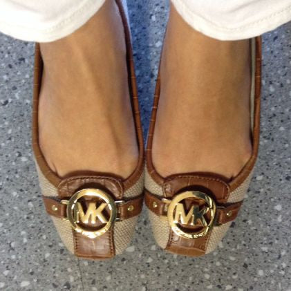Brown and beige flats with gold logo on a gray floor