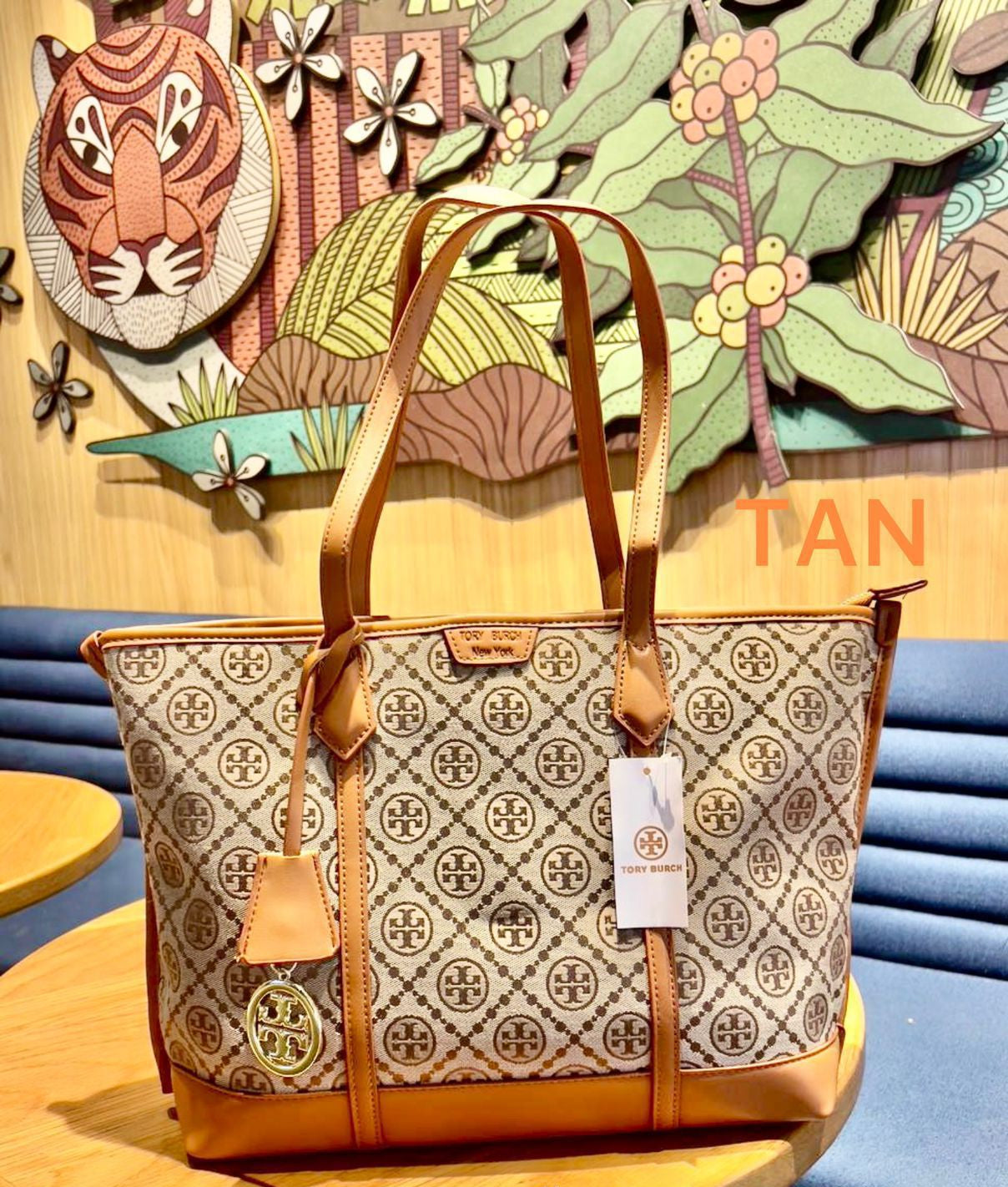 Designer handbag with brand tag on a wooden table against a colorful wall.