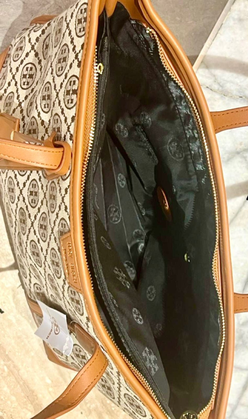 Open handbag with patterned exterior and black interior on a marble surface