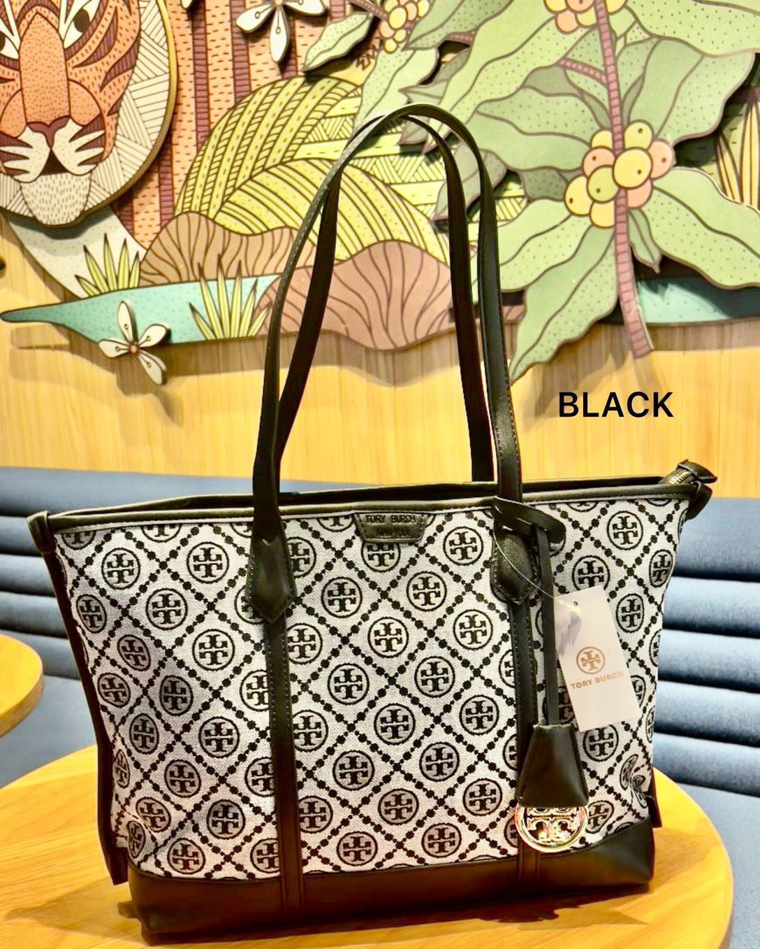 Black and white patterned handbag on a wooden table with decorative wall art in the background.