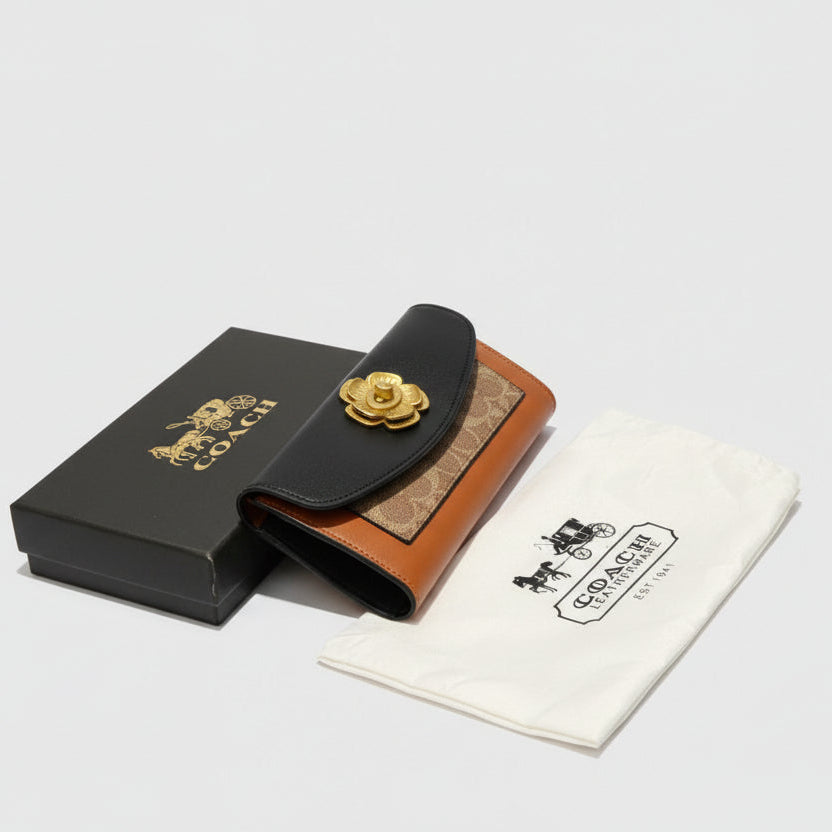 Coach wallet with gold emblem on a wooden table, surrounded by branded items.