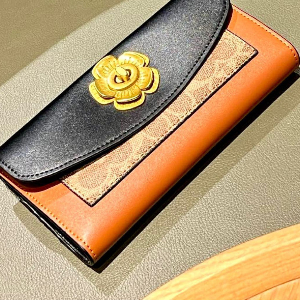 Coach wallet with gold flower emblem on a beige surface