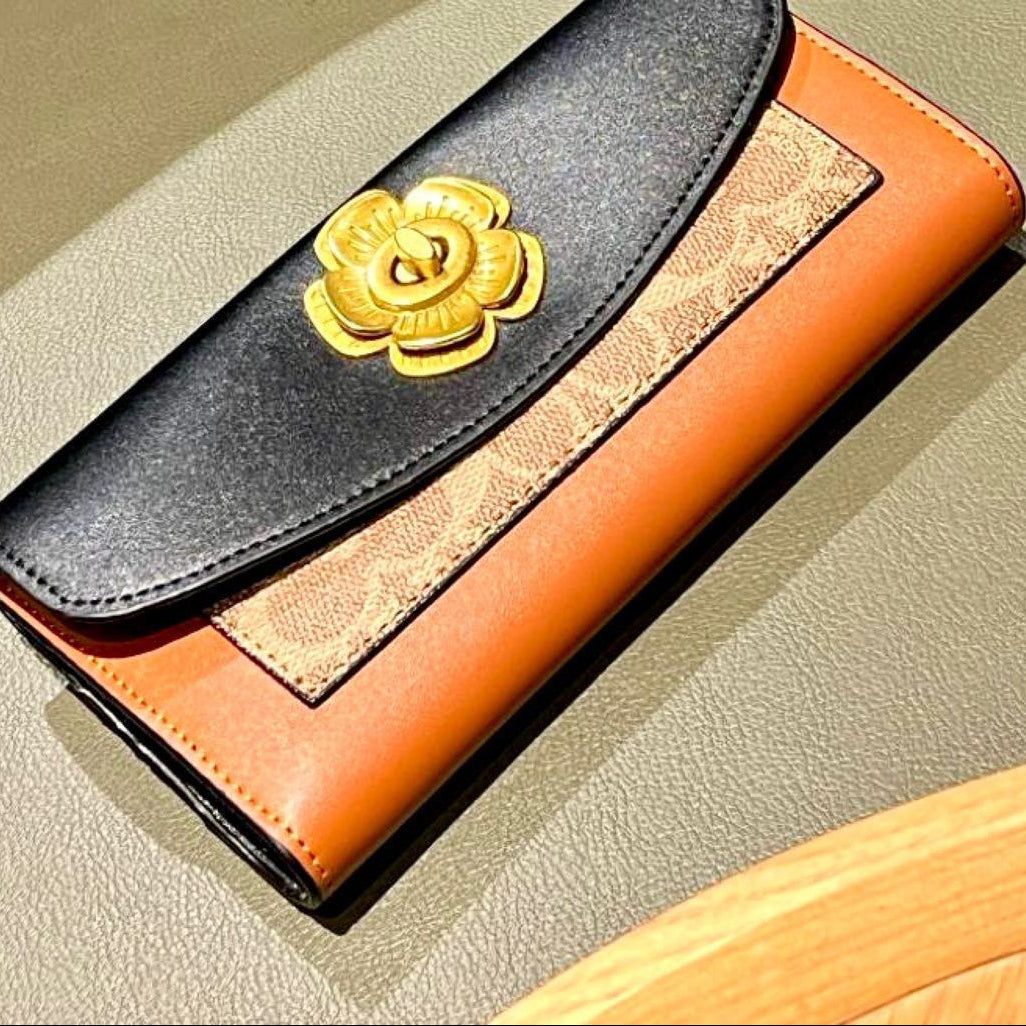 Coach wallet with gold flower emblem on a beige surface