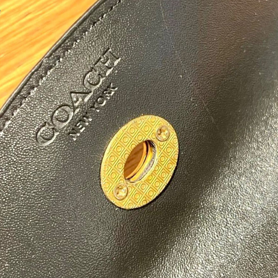 Close-up of a Coach product with gold emblem on a gray background