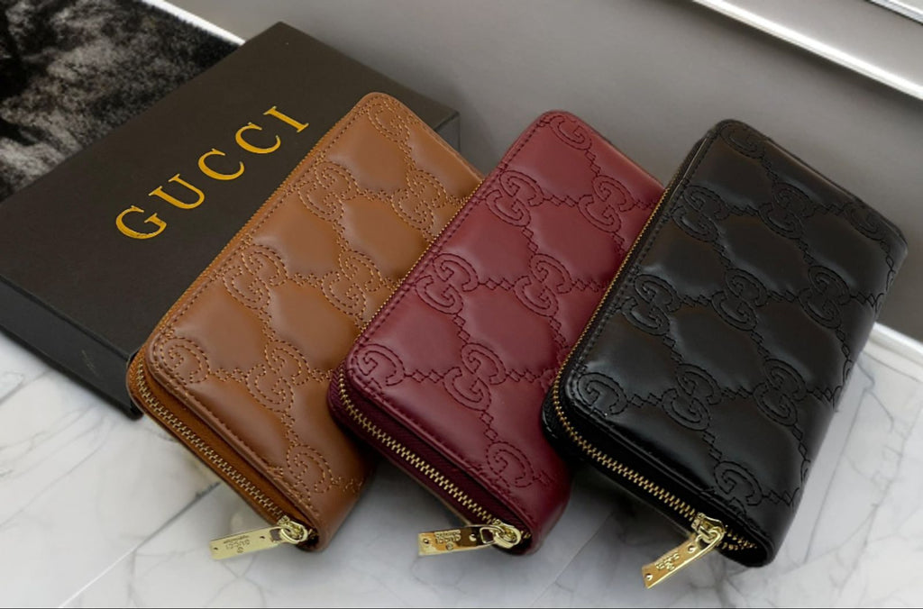 Three Gucci wallets in brown, red, and black on a marble surface with a Gucci box.