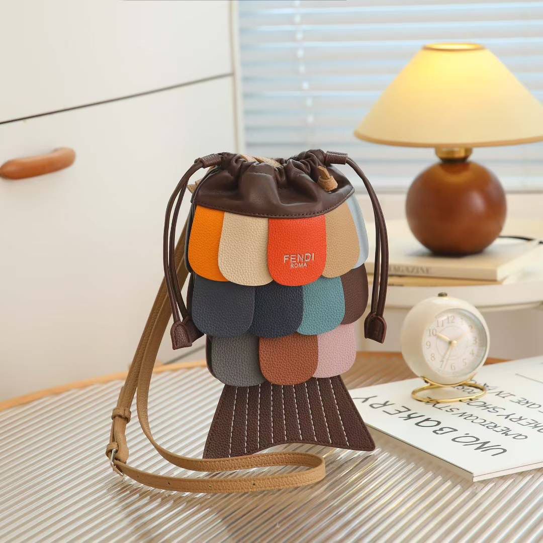 Tan Fendi Fish Sling Bag Fendi handbag with colorful patchwork design on a table with a lamp and books in the background.