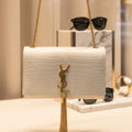 White handbag with gold chain and tassel on a neutral background