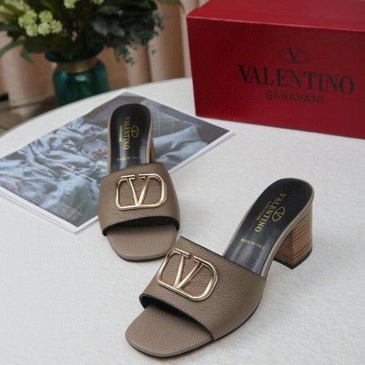 Brown sandals with gold logo on a white surface next to a red Valentina box.