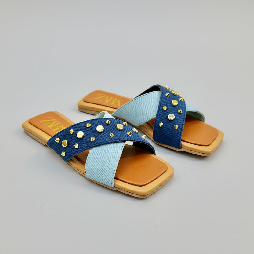 Zara sandals with blue straps and gold studs on a wooden surface with Zara packaging.
