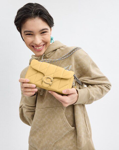 Person holding a Beige Coach tabby quilted handbag with a chain strap on a white background