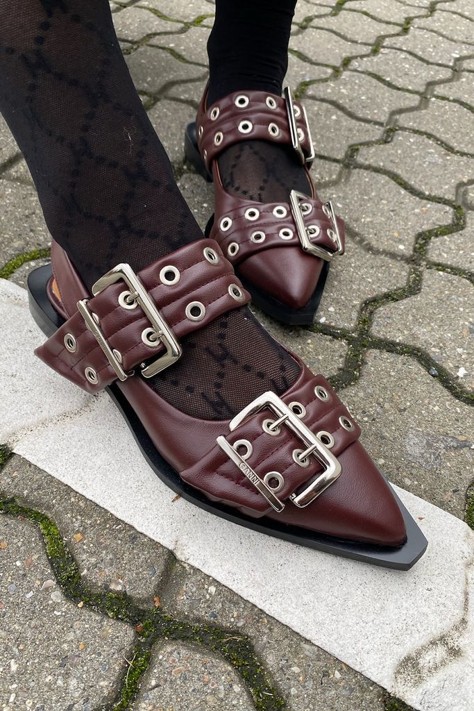 Tan CHLOÉ Western Look Footwear pointed-toe shoes with silver buckles worn on a stone ledge.