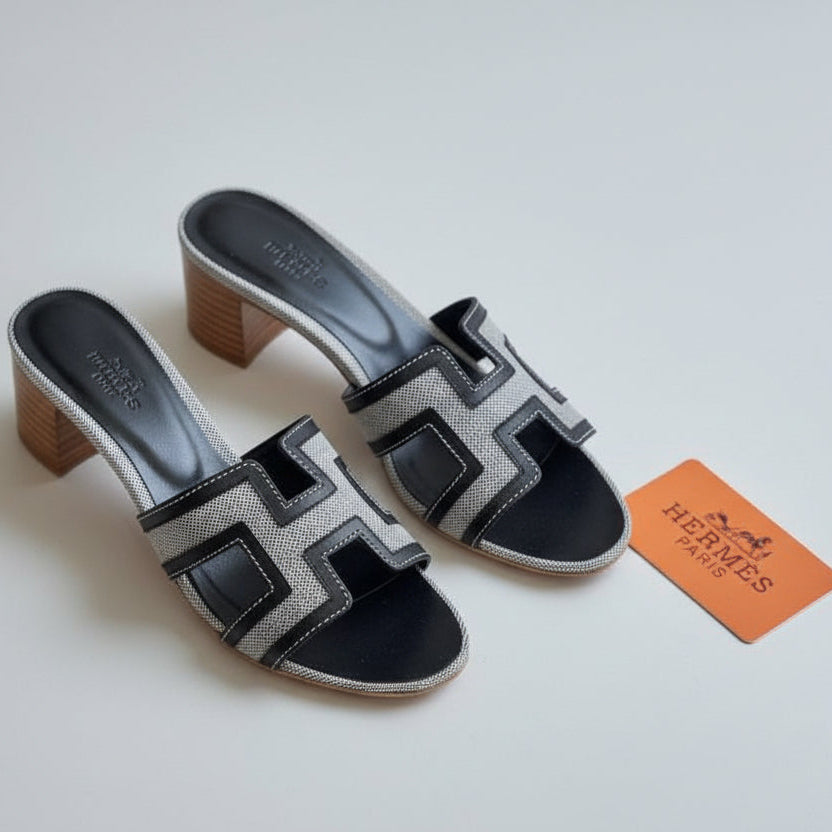 Black HERMES Heel and white patterned sandals with a visible brand logo on a white surface.