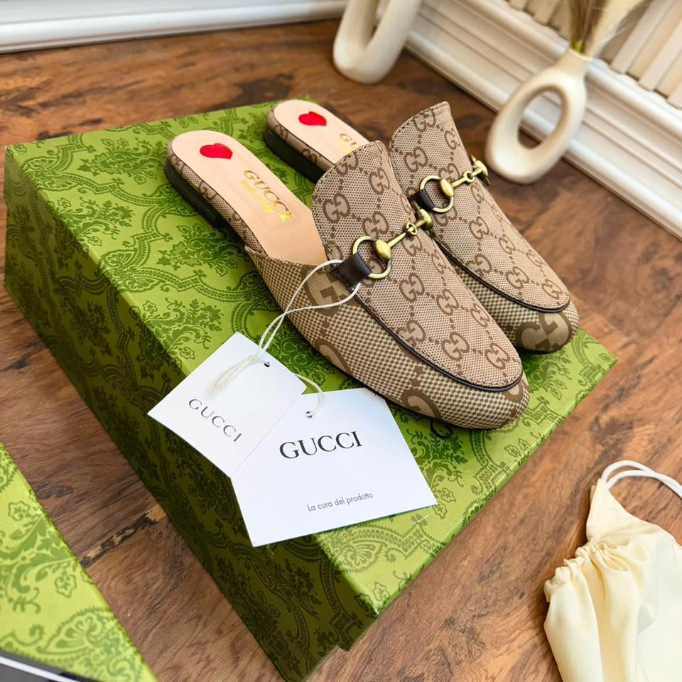 Brown Gucci loafers on a green box with a Gucci tag, on a wooden surface.