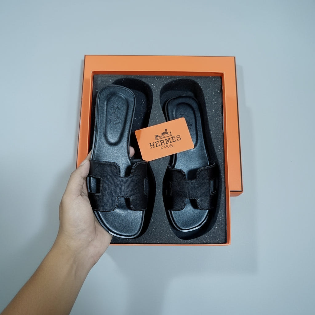 Black sandals in a Hermès box on a desk with office items.
