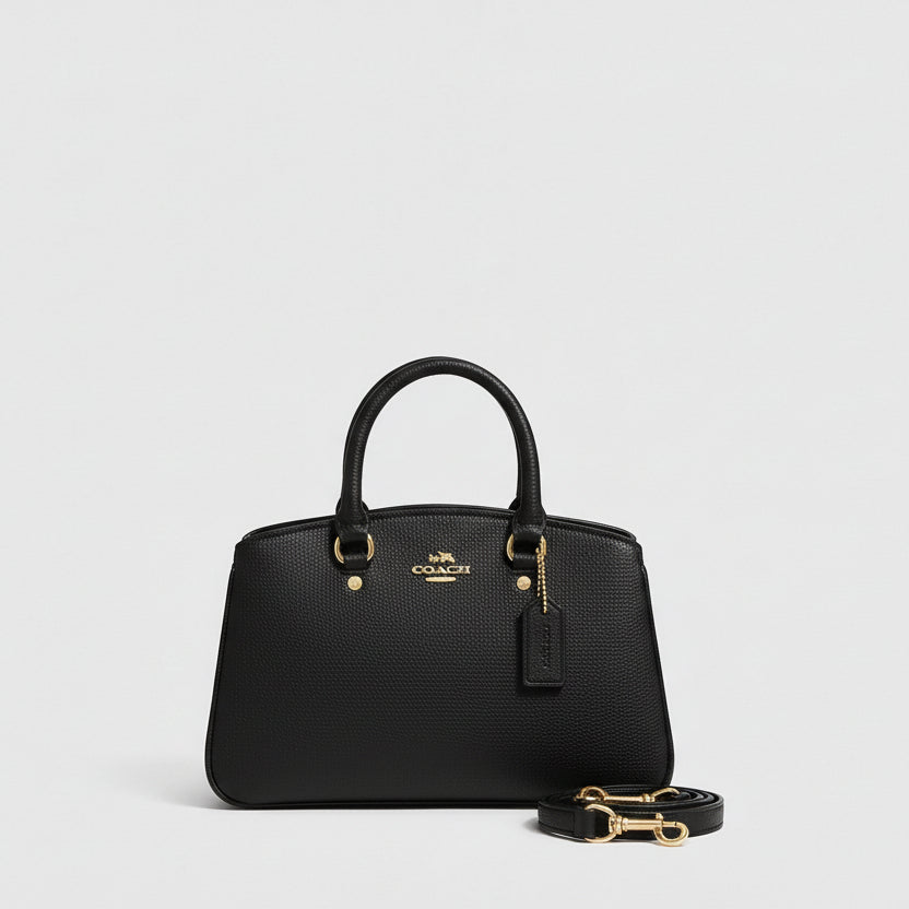 Black Coach Savannah Carryall Bag  handbag on a white surface with a plant and packaging in the background.