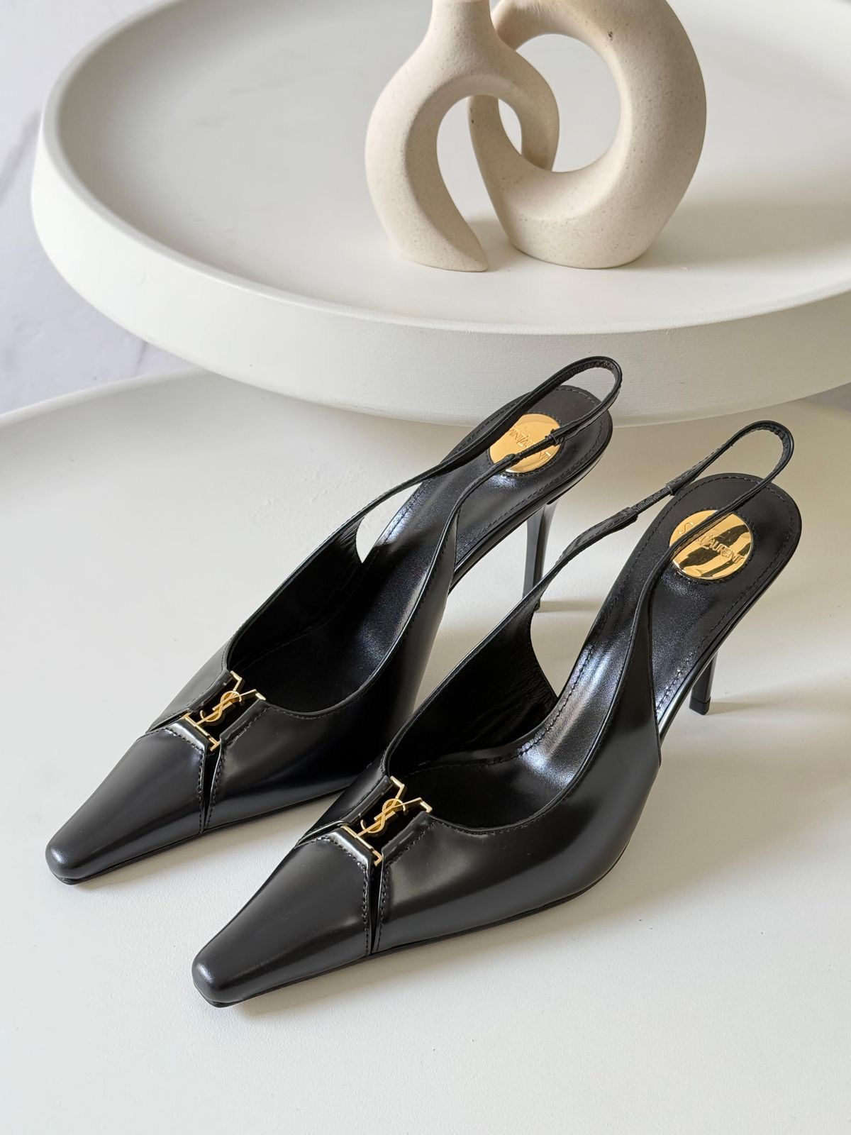 YSL Babylone Women’s Pumps Black high-heeled shoes with gold accents on a white surface
